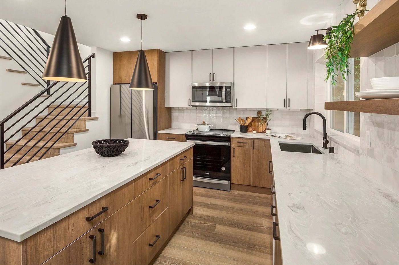 Kitchen with a white island, walnut cabinets and black pendants