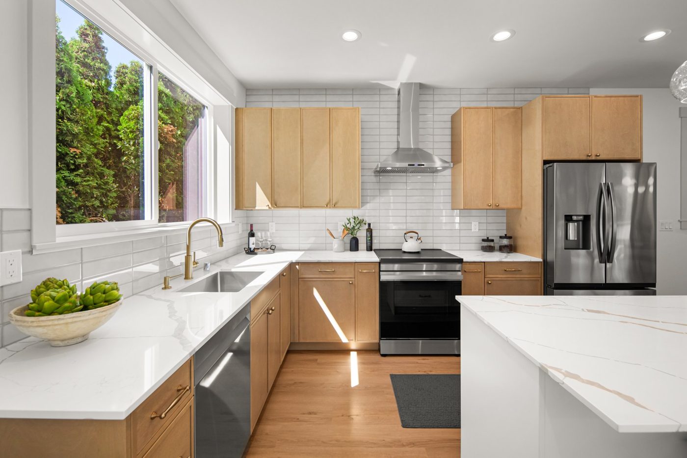 Kitchen with light oak cabinets, a marble-look island and a stainless range