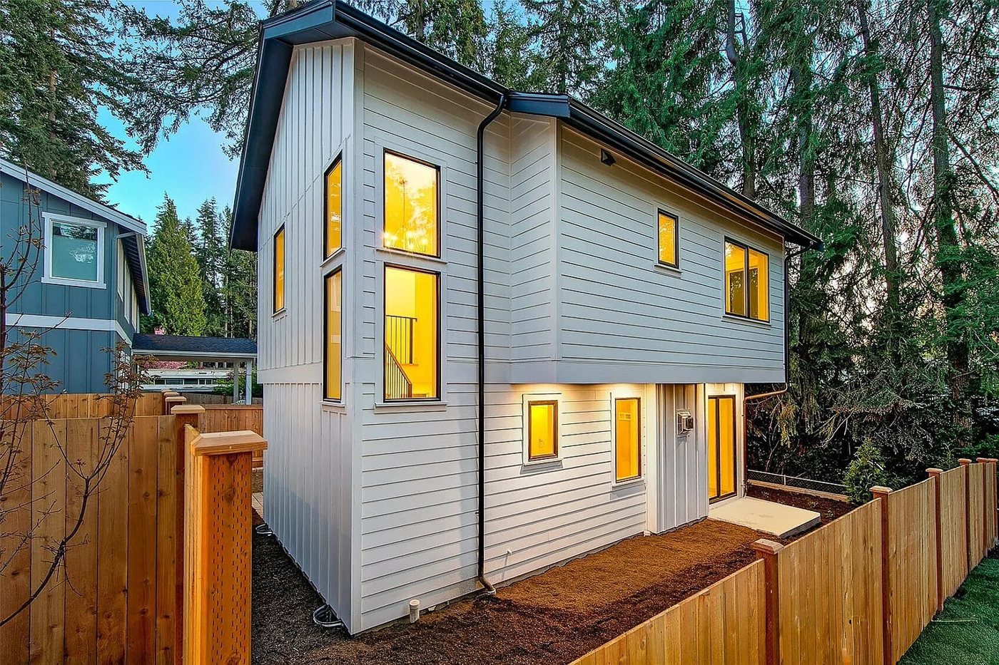 Two-level white lap-sided backyard home at dusk behind a cedar fence, Kirkland