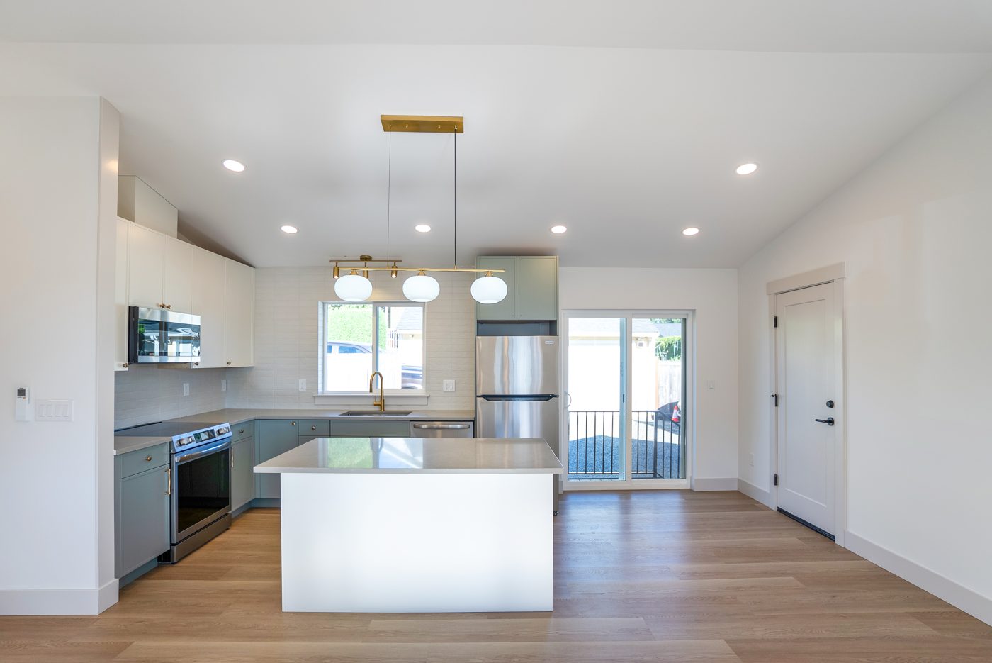 Kitchen with a white island, sage cabinets and brass fixtures under a vaulted ceiling